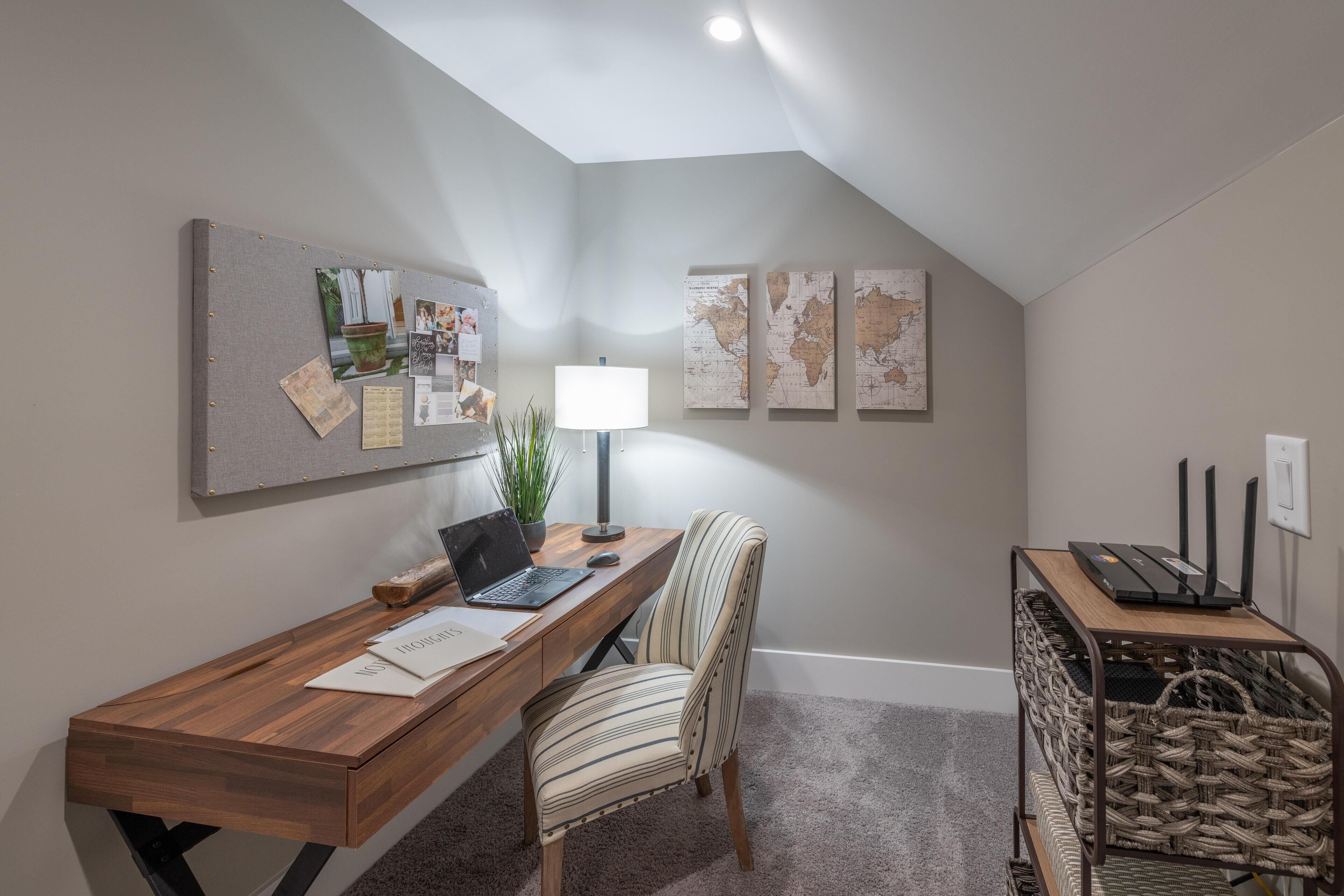 A home office with a desk, two chairs, a laptop, a lamp, and a wall-mounted map.