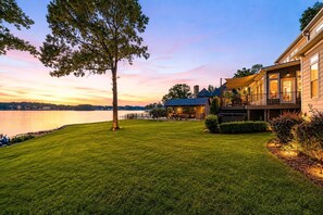 A waterfront property with a well-maintained lawn, a large tree, and a building with a balcony overlooking the water.