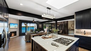 A modern kitchen with a large island, dark cabinetry, and a view of a lake. - Channel Marker (Mooresville)