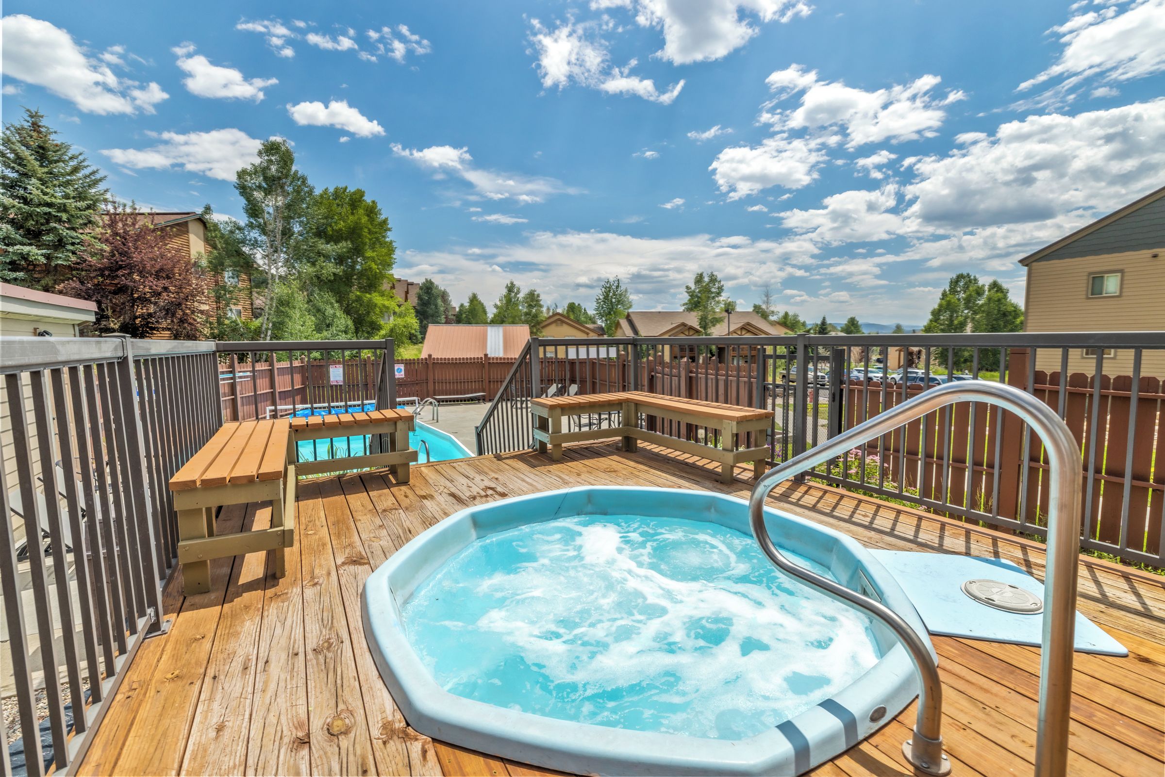 Une terrasse en bois avec un jacuzzi, une piscine et une clôture en bois.