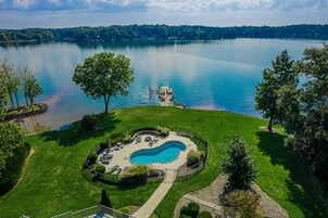 A swimming pool surrounded by a well-maintained lawn, with a dock extending into a lake.