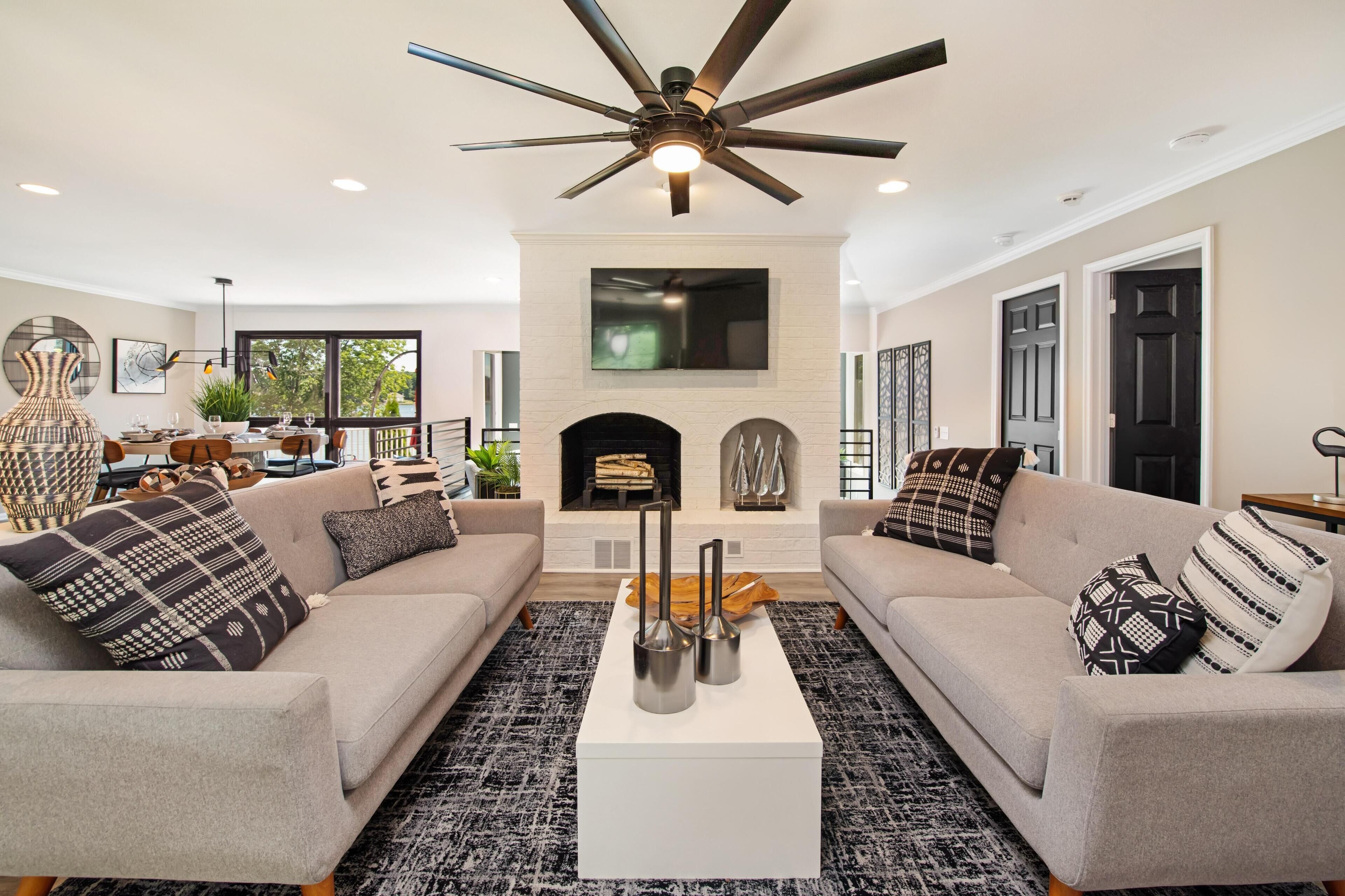 A modern living room with two sofas, a coffee table, a fireplace, and a ceiling fan.
