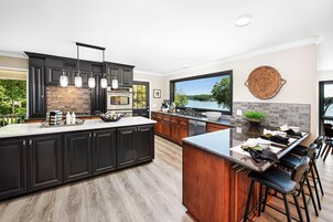 A modern kitchen with dark cabinetry, a large island, and a view of a lake.