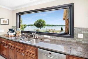 A kitchen with a large window, granite countertop, stainless steel sink, Bosch dishwasher, and wooden cabinets.