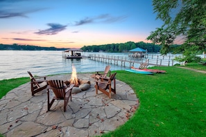 A stone patio with Adirondack chairs and a fire pit, overlooking a lake with docks and boats. - Normandy Approach (Mooresville)
