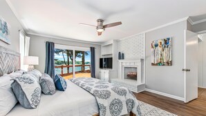 Ein Schlafzimmer mit Bett, Deckenventilator, Fernseher, Kamin und Blick ins Freie.