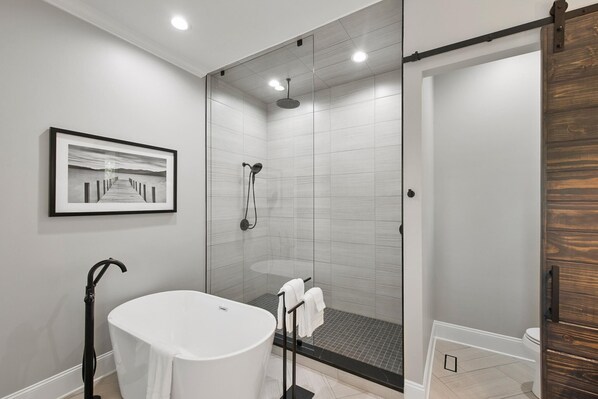 A modern bathroom with a glass-enclosed shower, a white bathtub, and a wooden door. - Paradise Peninsula (Mooresville)