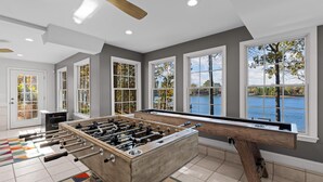 A spacious room with a foosball table, large windows with a lake view, and a ceiling fan. - Hillstone Ridge (Mooresville)