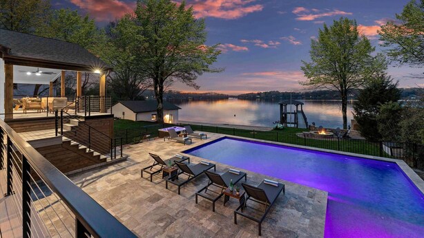 A swimming pool with lounge chairs, a deck area with a fire pit, and a view of a lake at dusk. - Keenan Beach W/beach, Heated Pool & Game Room (Mooresville)