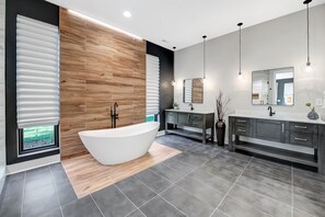 A modern bathroom with a freestanding bathtub, dark gray cabinetry, and a large mirror above the vanity. - Shoreline on Stonemarker (Mooresville)
