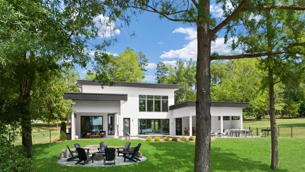 A modern two-story house with a patio area featuring outdoor furniture.