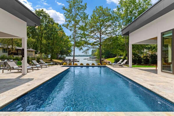 A modern outdoor swimming pool with lounge chairs and a view of a lake. - Shoreline on Stonemarker (Mooresville)