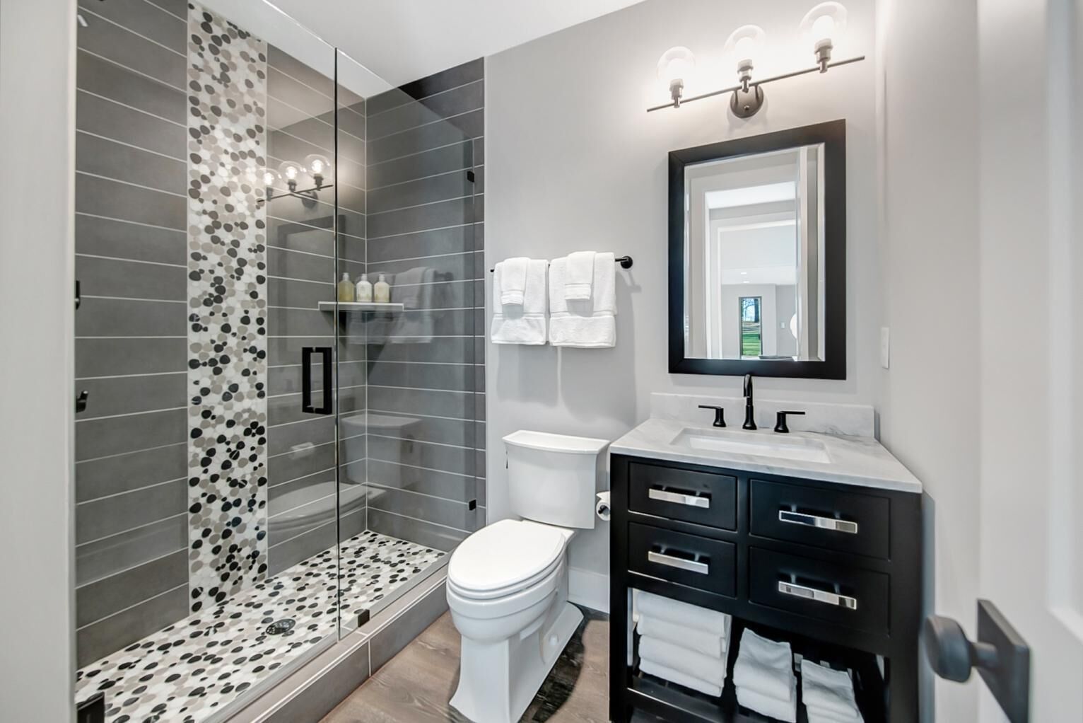 Et moderne badeværelse med en glasbrusekabine, toilet, håndvask og et skab med skuffer.