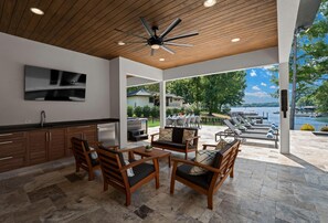 An outdoor patio with wooden furniture, a ceiling fan, and a view of a lake and boats. - Shoreline on Stonemarker (Mooresville)