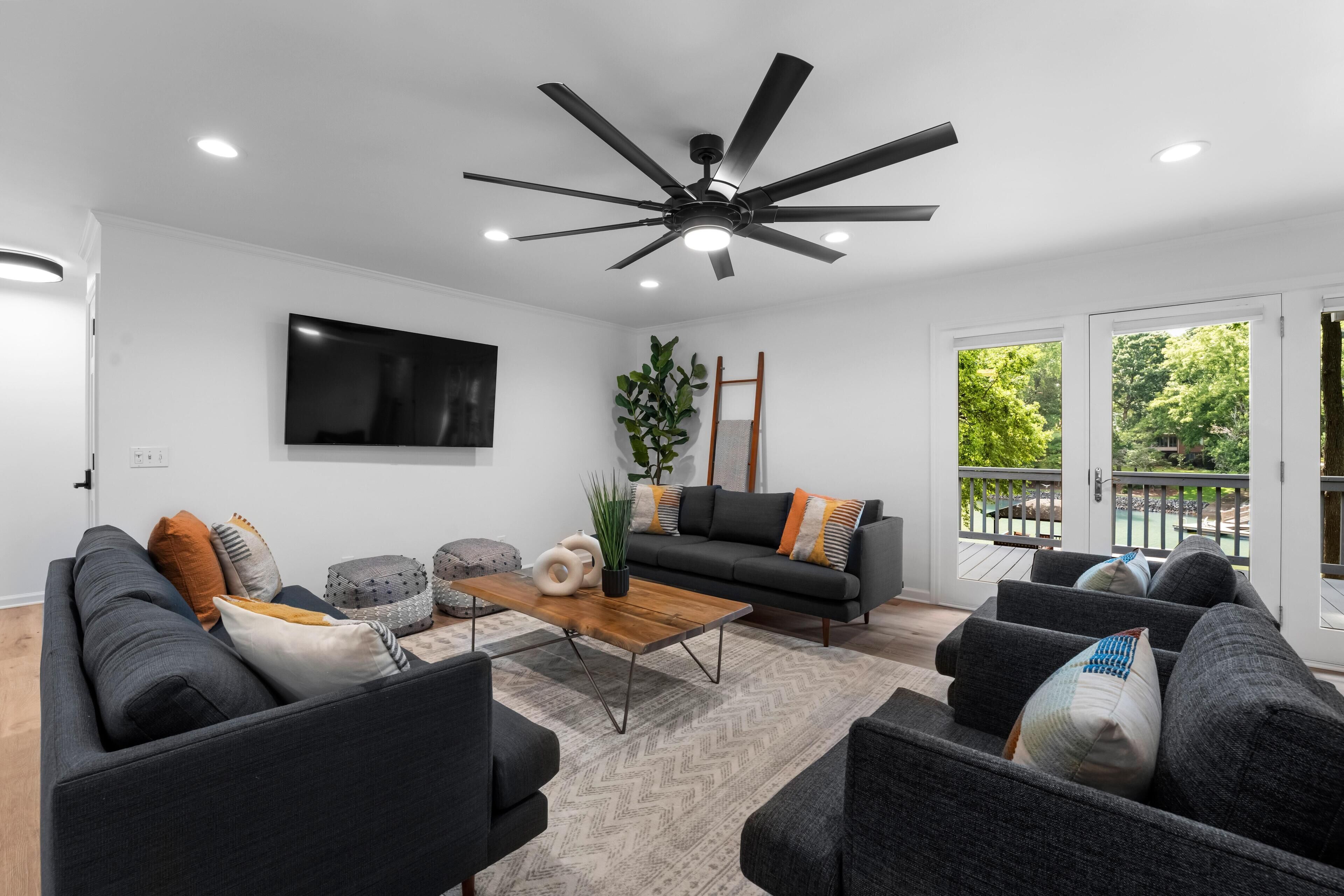 A modern living room with a ceiling fan, a flat-screen TV, a sofa set, a coffee table, and a potted plant.