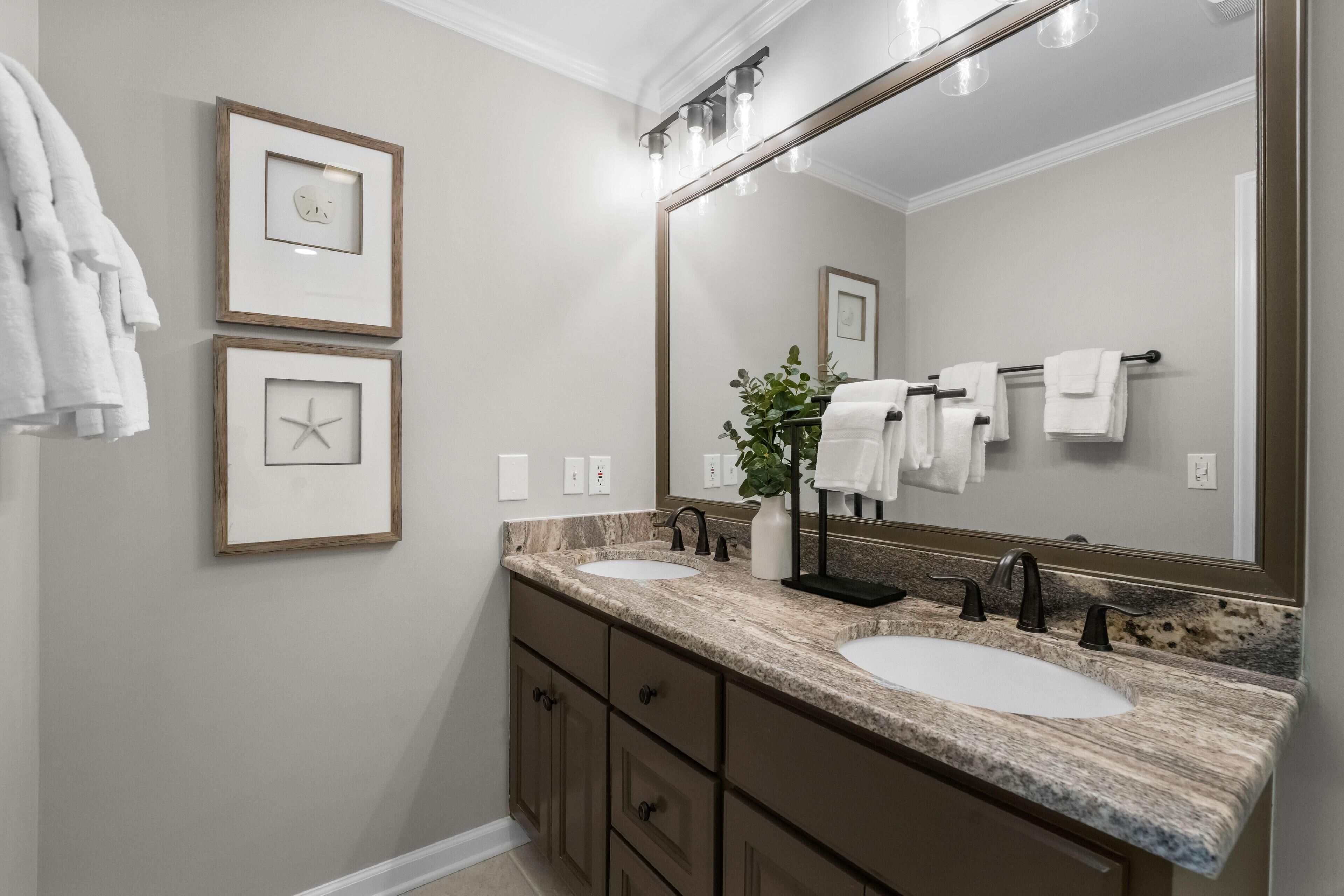 A bathroom with two sinks, a large mirror, framed pictures on the wall, and a towel rack.