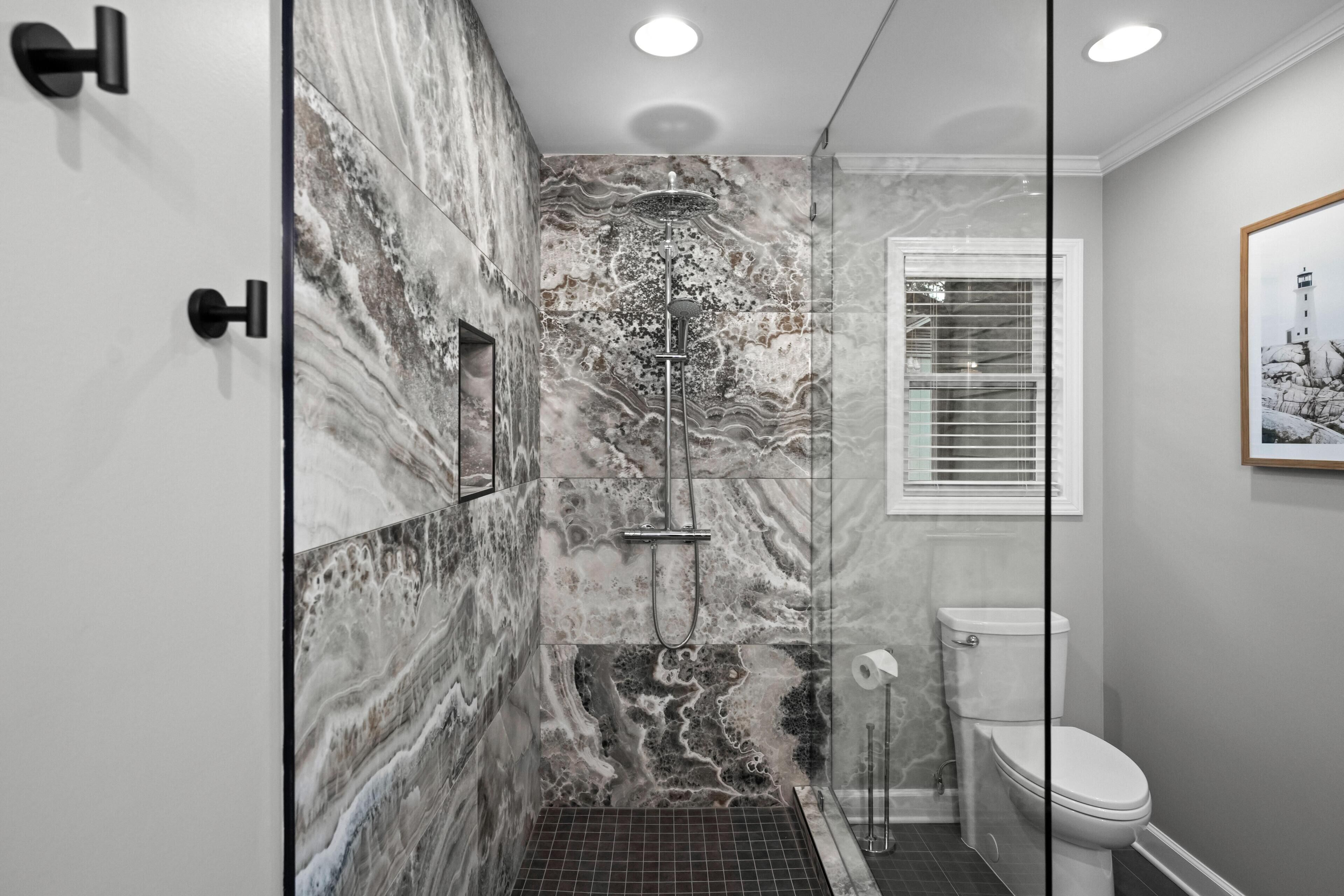 Ein modernes Badezimmer mit einer Duschkabine aus Glas, Marmorwänden, einer weißen Toilette und einem gerahmten Bild an der Wand.