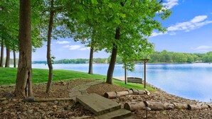 Ein steiniger Weg führt zu einem Gazebo an einem See, umgeben von Bäumen und einer Rasenfläche.