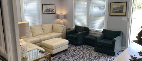 A living room with a beige sectional sofa, two dark armchairs, a glass coffee table, and a patterned rug.
