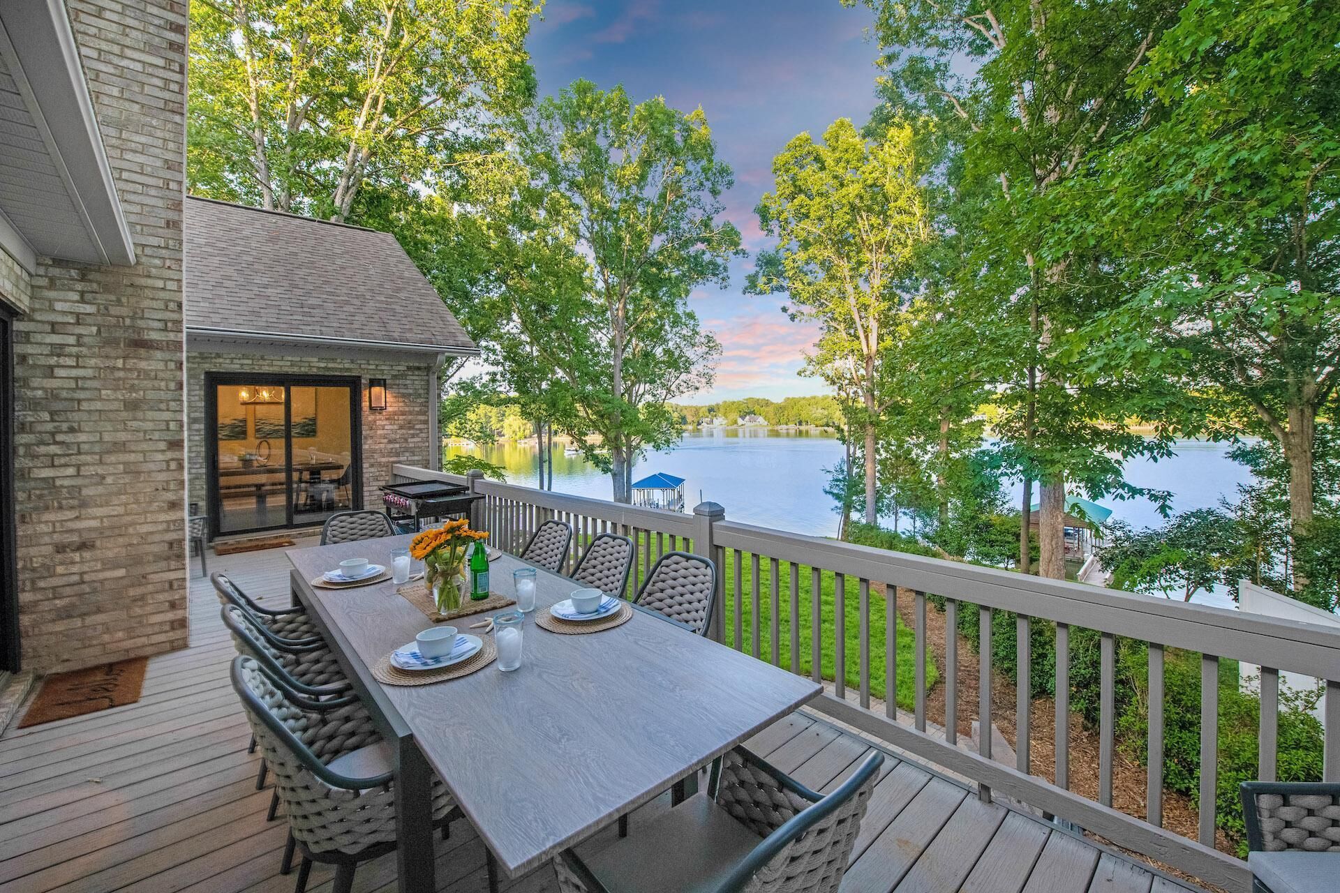 A deck with a table set for dining, overlooking a lake with trees and a gazebo.