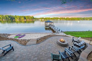 Un patio junto al lago con una chimenea, asientos y kayaks.