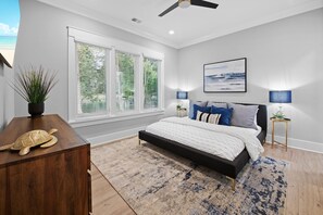 A bedroom with a bed, bedside lamps, a ceiling fan, a window with blinds, and a view of the outdoors. - Hanesbee Escape (Mooresville)