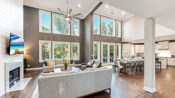 Amplia sala de estar con chimenea, ventanas grandes y una zona de comedor con una cocina al fondo.