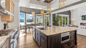 A spacious kitchen with a large island, wooden cabinets, and a modern chandelier. - Mallard Vestige (Denver)