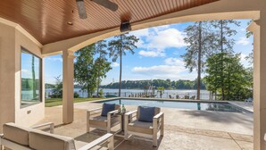 A covered patio with outdoor furniture, a pool, and a view of a lake and trees. - Mallard Vestige (Denver)