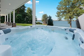A hot tub with a view of a lake, surrounded by a covered patio with stone pillars and outdoor furniture. - Strawpocket to Starboard (Mooresville)