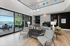 A modern living room with a large glass door leading to an outdoor patio, a fireplace, and a view of the water. - Strawpocket to Starboard (Mooresville)