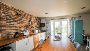 A kitchen with a brick wall, wooden table, and chairs, a blue refrigerator, and a window with curtains. - 50 Harbour Road (Bognor Regis)