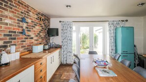 A kitchen with a brick wall, a wooden countertop, a television, and a teal refrigerator. - 50 Harbour Road (Bognor Regis)