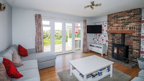 A living room with a sofa, a coffee table, a fireplace, a television, and a sliding glass door leading to an outdoor area. - 50 Harbour Road (Bognor Regis)
