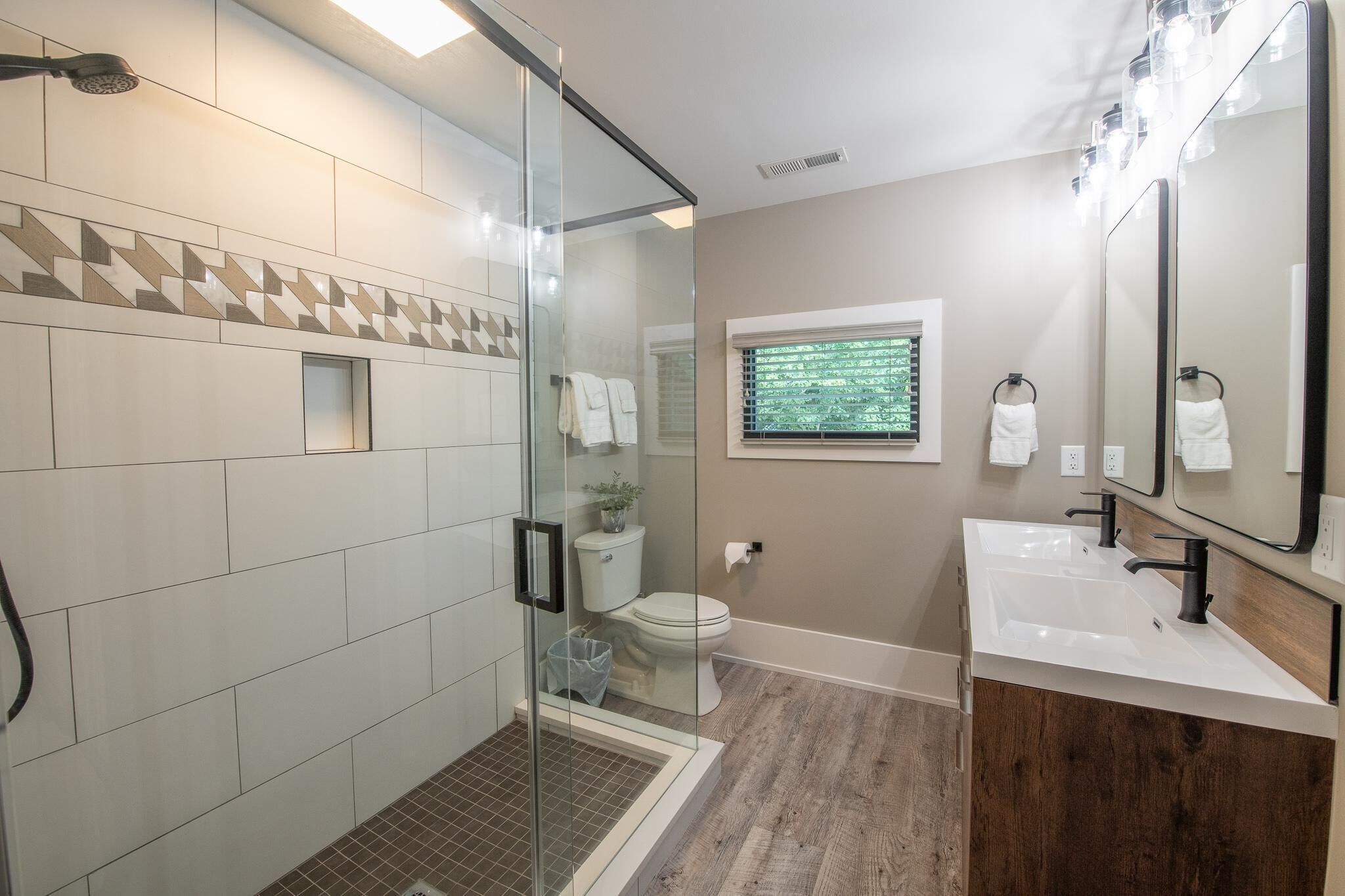 A modern bathroom with a glass shower enclosure, a toilet, and a sink with a mirror.