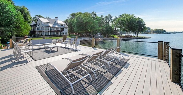 Une terrasse au bord du lac, avec des sièges d’extérieur, et une maison en arrière-plan.