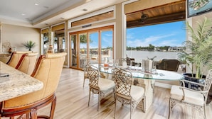 Un coin repas avec une table en verre, des chaises en osier et une vue sur un plan d’eau.