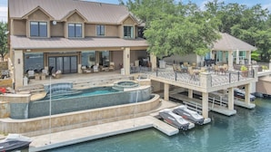 Une grande maison avec une piscine, un espace extérieur aménagé et un quai avec des bateaux.