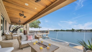 Un espace extérieur abrité, aménagé avec des meubles en osier, une table en bois sur laquelle sont disposées des boissons, et offrant une vue sur un lac.