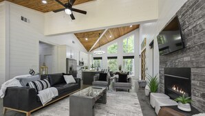 A spacious living area with a fireplace, a sofa, a coffee table, and a kitchen in the background. - Summerwoods: Sleeps 8 | Fire Pit | Hot Tub | EV (Broken Bow)