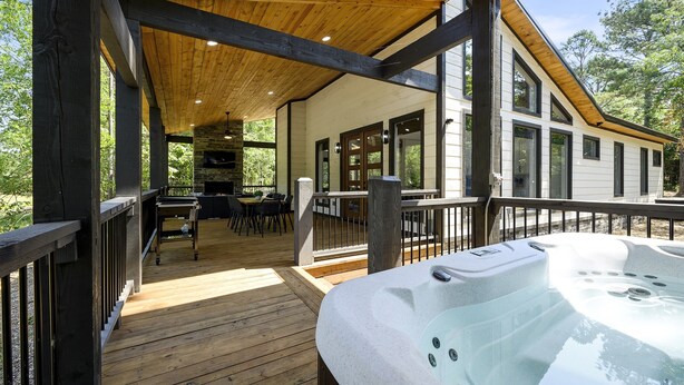 A wooden deck with a hot tub, outdoor seating, and a view of the house. - Summerwoods: Sleeps 8 | Fire Pit | Hot Tub | EV (Broken Bow)
