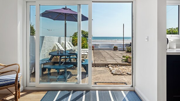 Una stanza con una porta scorrevole in vetro che dà su un patio con tavolo, sedie e ombrellone.