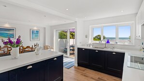 Una cucina moderna con mobili scuri, un piano di lavoro bianco e vista sul mare attraverso ampie finestre.