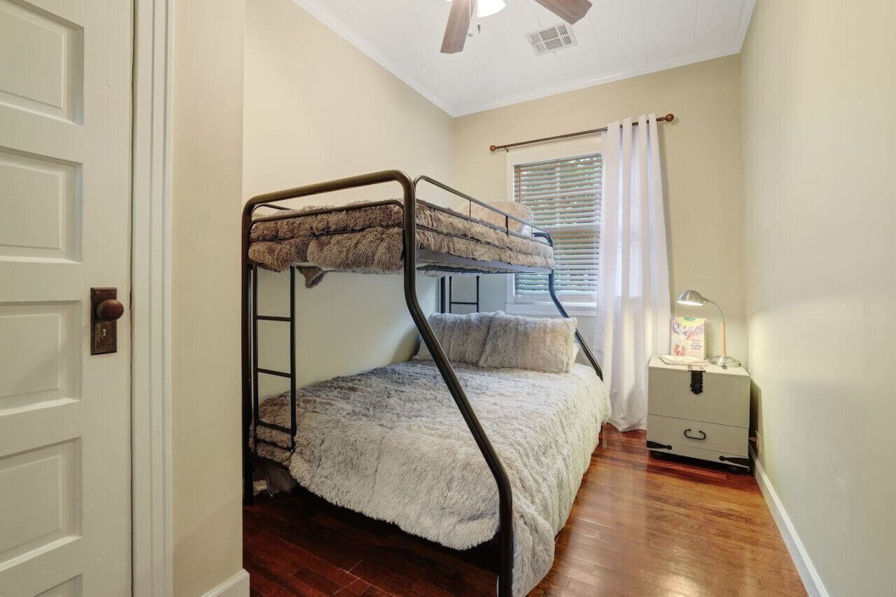 Un lit superposé dans une chambre équipée d’un ventilateur de plafond, d’une fenêtre avec des stores et d’une table de chevet avec une lampe.