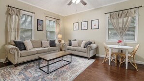 A living room with two beige sofas, a coffee table, a dining table with chairs, and a ceiling fan. - Main Street Charmer 3 Bedrooms (New Iberia)