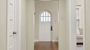 A hallway with a wooden floor, white walls, and a white door with a window. - Main Street Charmer 3 Bedrooms (New Iberia)
