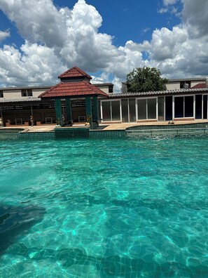 Ein Schwimmbecken mit klarem Wasser, ein Gazebo und im Hintergrund ein Gebäude mit rotem Dach.