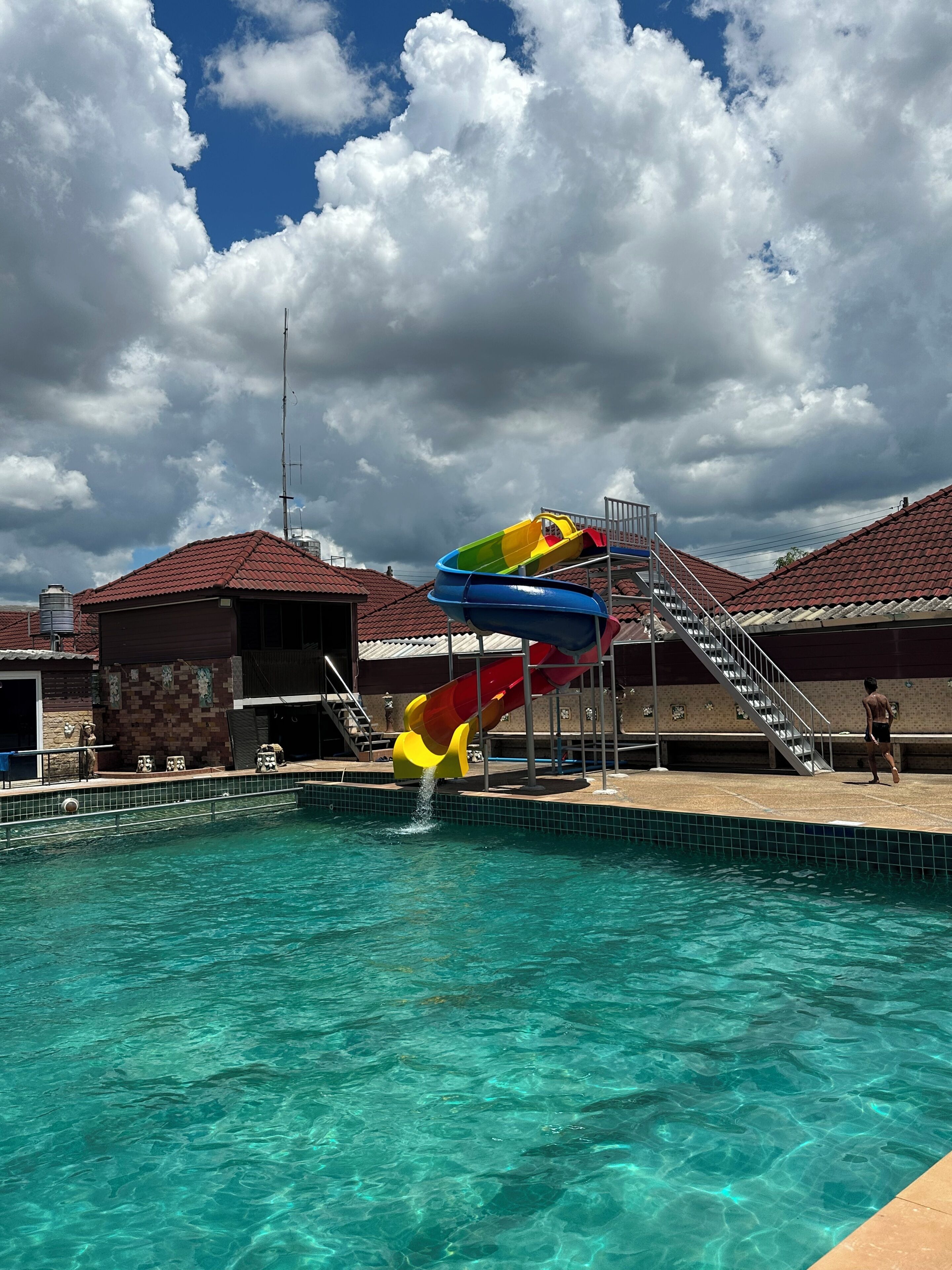 A swimming pool with a multi-colored water slide and a staircase leading to a roofed area.