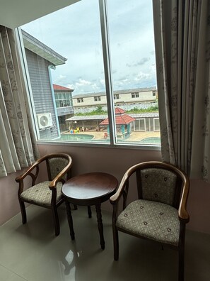 Ein Zimmer mit großem Fenster, zwei Holzstühlen, einem kleinen runden Tisch und einer Klimaanlage.