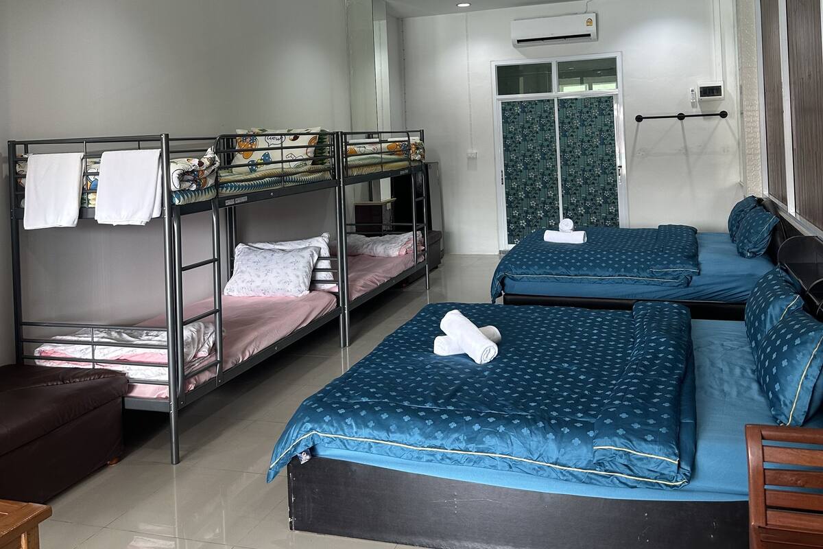 A dormitory-style room with bunk beds, a small seating area, and a door leading to a bathroom.